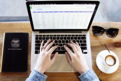 Mujer frente a una computadora completando un formulario en línea del SEPE, con carpetas y una taza de café sobre la me…
