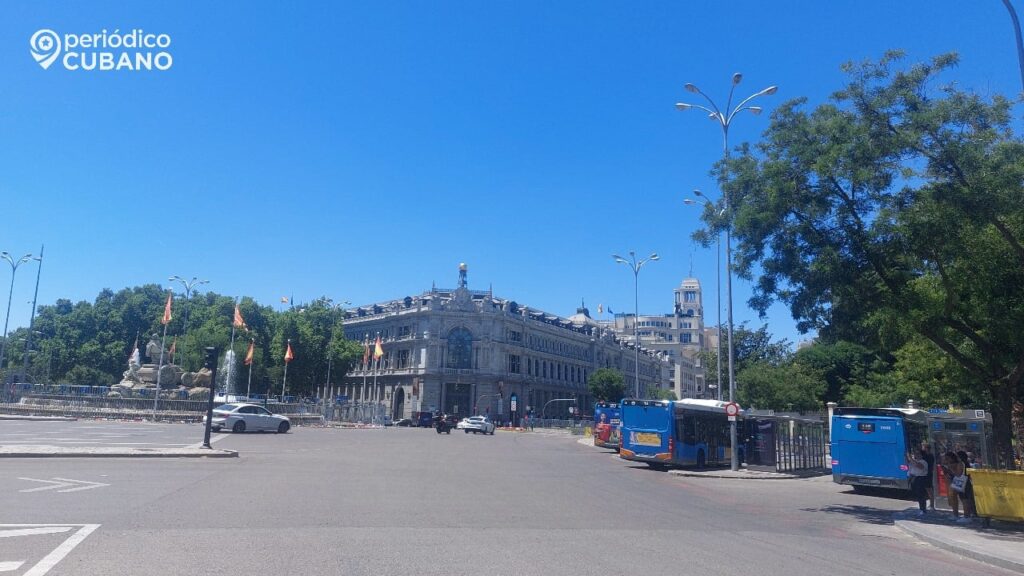 Persona revisando documentos frente a un ordenador portátil, con banderas de España y otro país al fondo. Concepto de P…