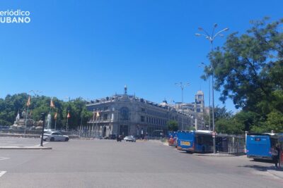 Persona revisando documentos frente a un ordenador portátil, con banderas de España y otro país al fondo. Concepto de P…